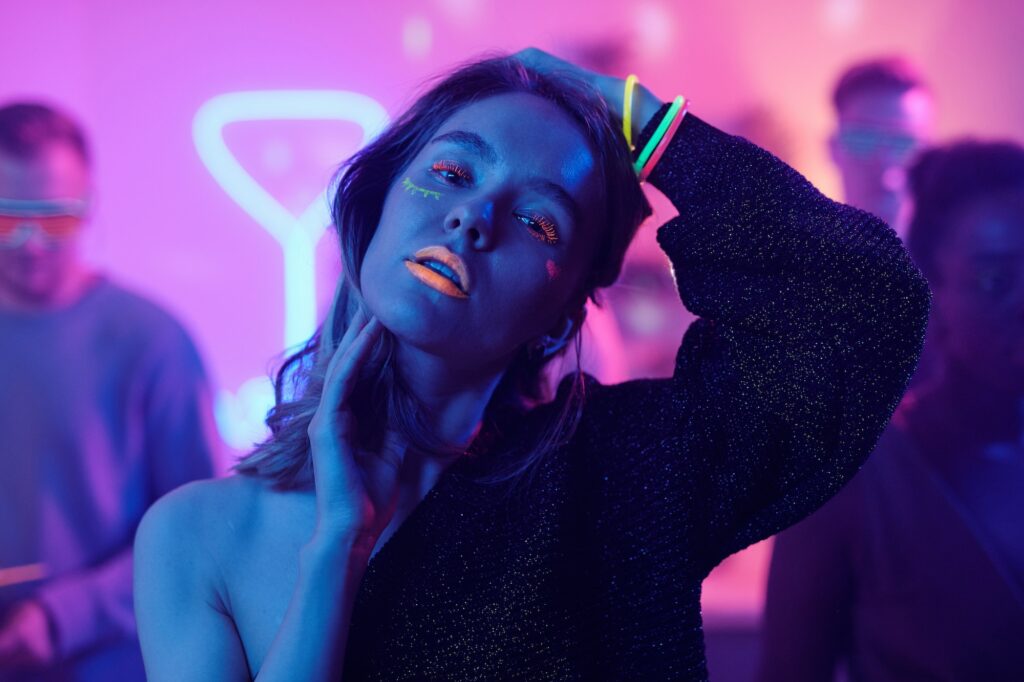 Young woman with glamorous neon makeup standing against her friends at party